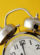 old fashioned chrome alarm clock set against warm yellow background